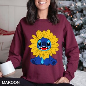 A woman wearing a maroon sweater with a cartoon character of a blue creature with a yellow flower on it.