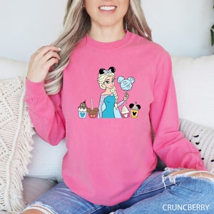 a woman sitting on a couch wearing a pink sweatshirt