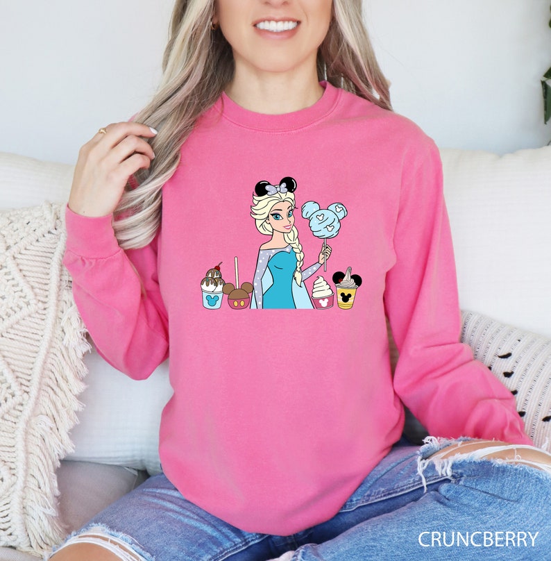 a woman sitting on a couch wearing a pink sweatshirt