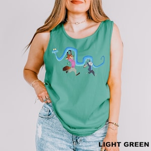 A woman wearing a green tank top with a cartoon character design and jeans stands against a white background.