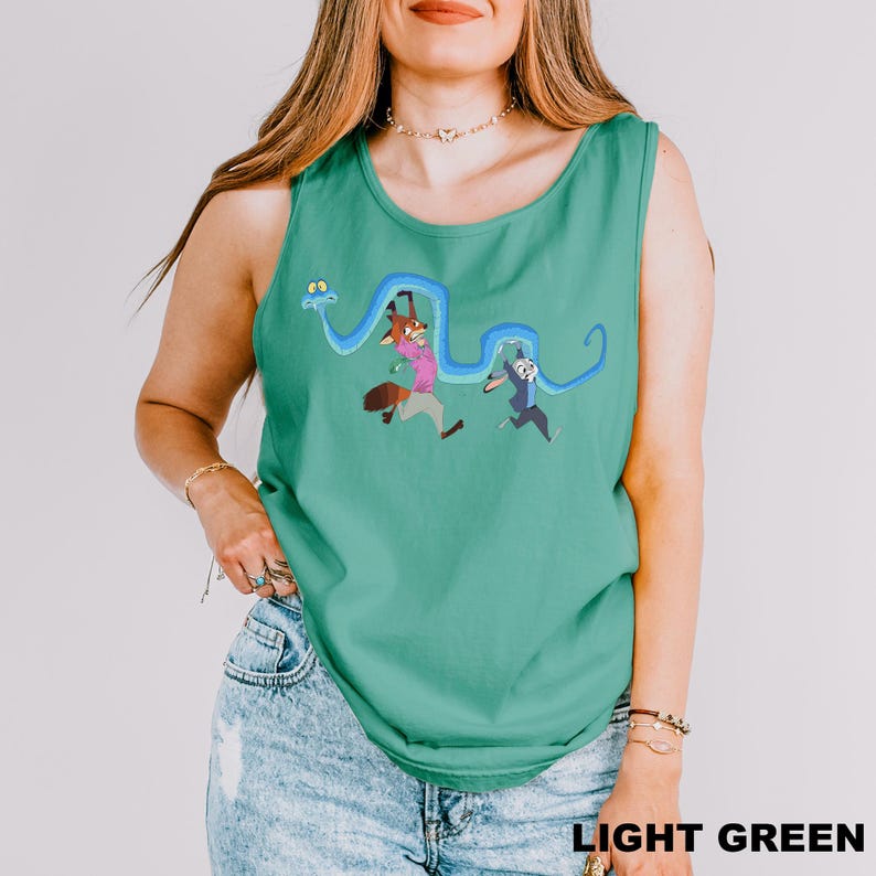 A woman wearing a green tank top with a cartoon character design and jeans stands against a white background.