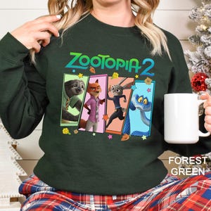 A woman wearing a green sweatshirt with a graphic of four cartoon animal characters from the movie Zootopia 2.