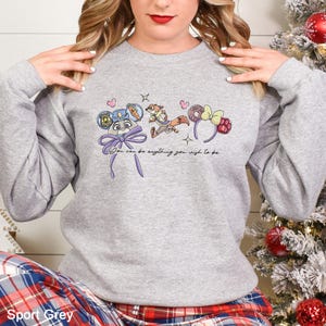 A woman wearing a gray sweatshirt with a graphic design featuring cartoon characters and text.