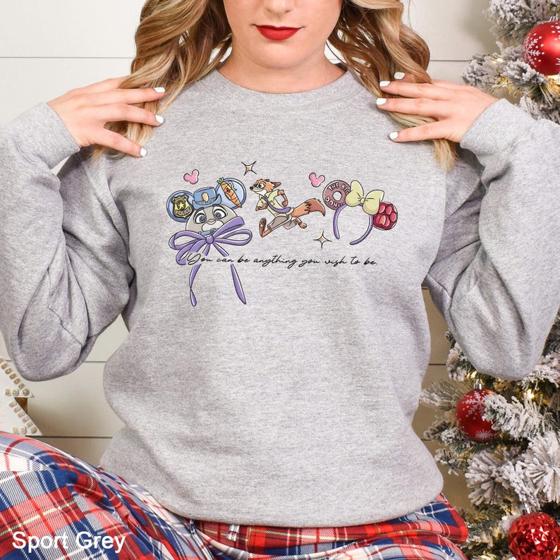 A woman wearing a gray sweatshirt with a graphic design featuring cartoon characters and text.