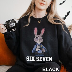 A woman wearing a black sweatshirt with a cartoon rabbit character and the text "SIX SEVEN" printed on it.