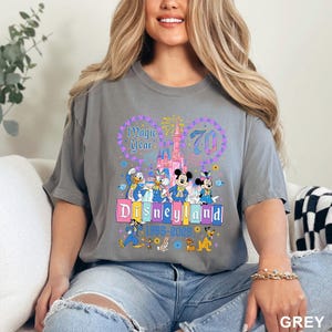A woman wearing a gray t-shirt with a Disney theme graphic and text, sitting on a couch.