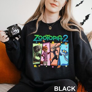 A woman wearing a black sweatshirt with a colorful graphic of the characters from the animated film "Zootopia 2" on it.