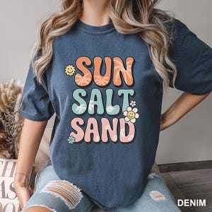 A woman wearing a blue t-shirt with the text "SUN SALT SAND" printed on it.