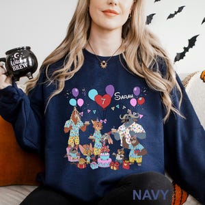 A woman wearing a navy blue sweatshirt with a graphic design of cartoon animals celebrating a birthday.