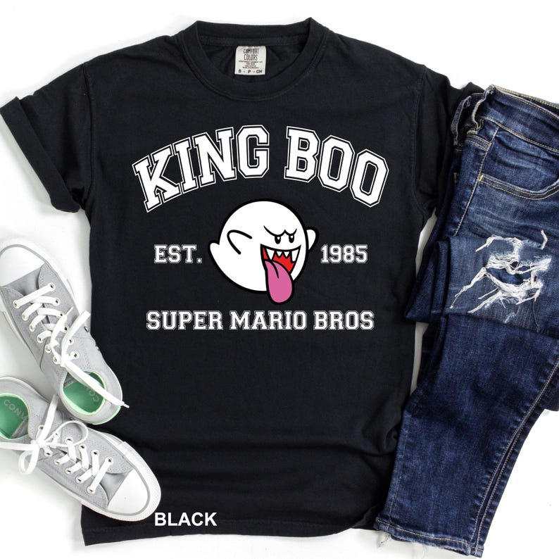 A black t-shirt with a graphic design featuring a ghost character and text, along with a pair of jeans and sneakers.