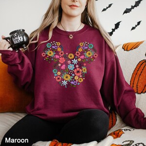 a woman sitting on a bed with a mickey mouse sweatshirt on