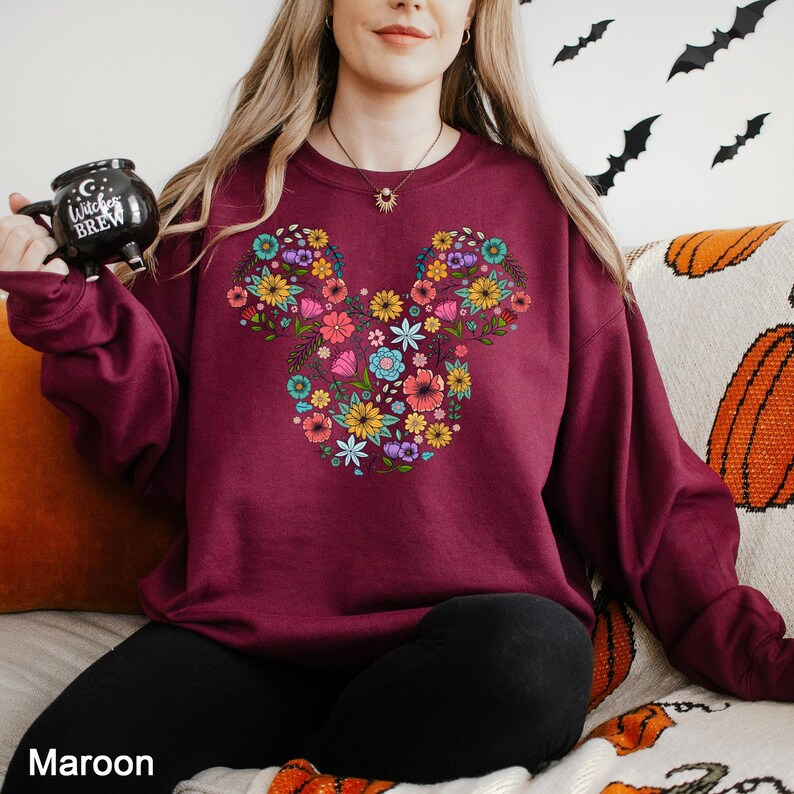 a woman sitting on a bed with a mickey mouse sweatshirt on