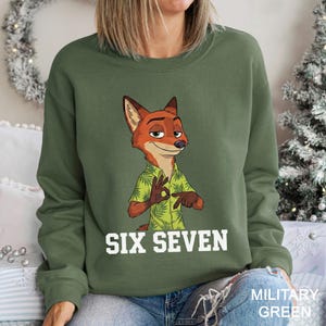 A woman wearing a green sweatshirt with a cartoon image of a fox and the text "SIX SEVEN" printed on it.