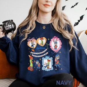 A woman wearing a navy blue sweatshirt with a cartoon character design, including a bunny, fox, and other animals. She is holding a black mug with a Halloween-themed design.