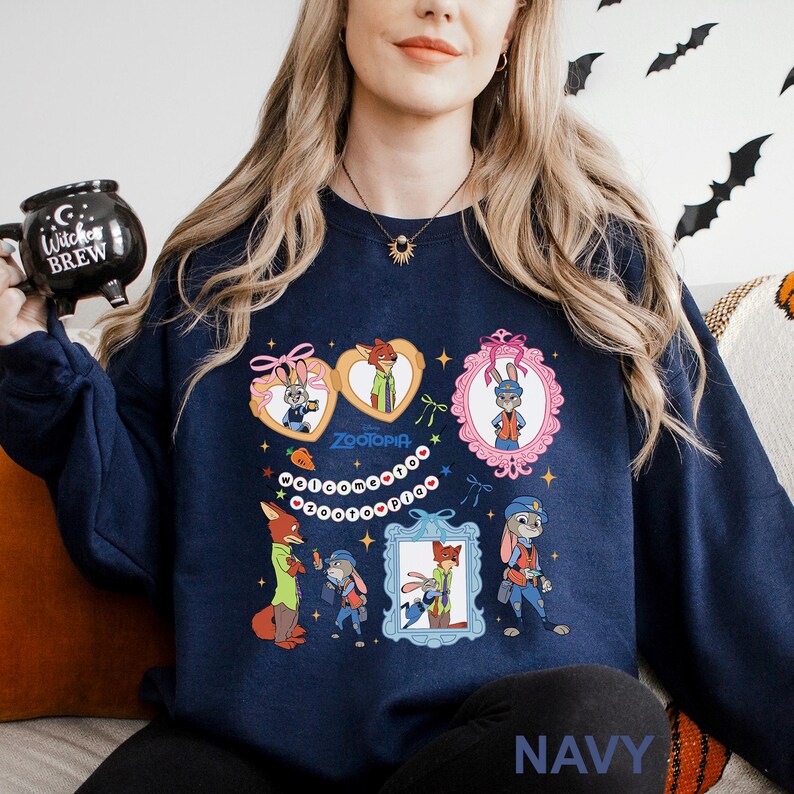 A woman wearing a navy blue sweatshirt with a cartoon character design, including a bunny, fox, and other animals. She is holding a black mug with a Halloween-themed design.