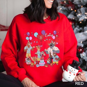 A woman wearing a red sweater with a cartoon illustration of a birthday party scene, including a snowman, balloons, and various animals.
