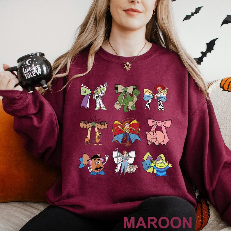 A woman wearing a maroon sweater with various cartoon characters printed on it, holding a black mug.