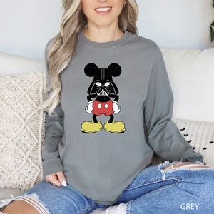 a woman sitting on a couch wearing a mickey mouse sweatshirt