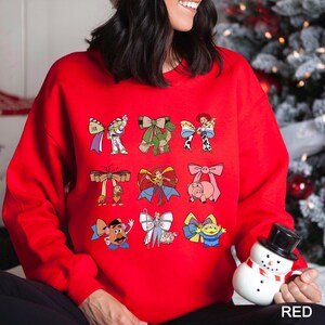 A woman wearing a red sweater with various cartoon characters on it, including a pig, a dog, and other characters, is holding a snowman and a toy.