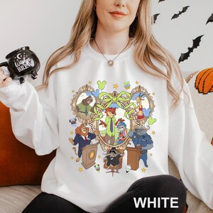 A woman wearing a white sweatshirt with a cartoon character design on it, holding a mug with a black design.