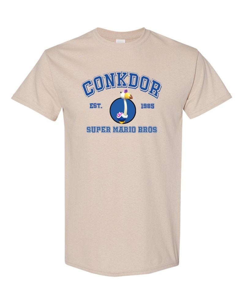 The image is a beige t-shirt with a graphic design featuring a blue circle with a yellow bird inside, and text above and below the circle.