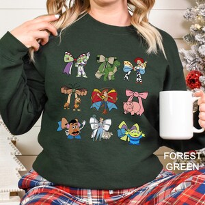 A woman wearing a green sweater with various cartoon characters printed on it, holding a white mug.