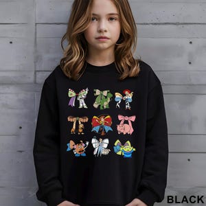 A young girl wearing a black sweatshirt with a graphic of various cartoon characters printed on it.