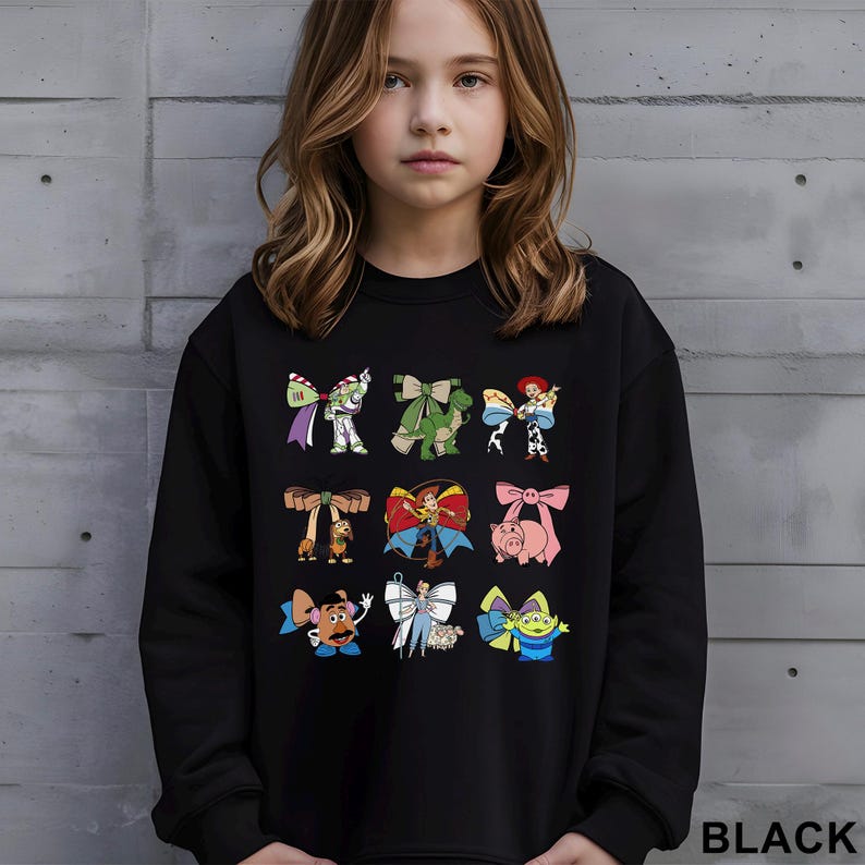 A young girl wearing a black sweatshirt with a graphic of various cartoon characters printed on it.