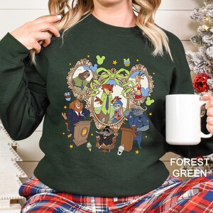 A woman wearing a green sweater with a colorful graphic design featuring various cartoon characters, including a lion, a mouse, and a police officer. She is holding a white mug in her hand.