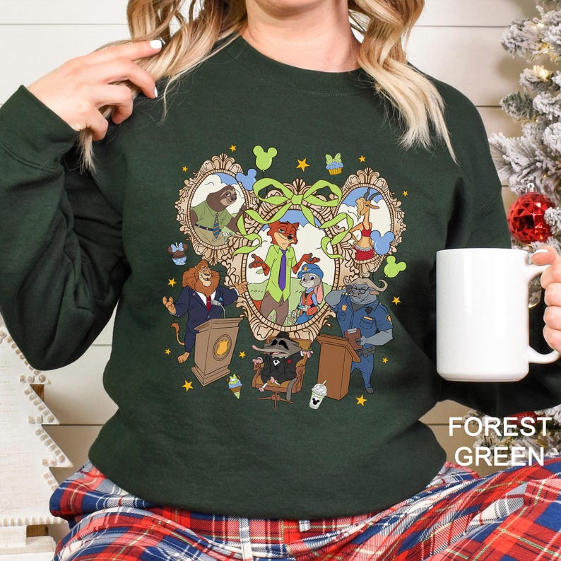 A woman wearing a green sweater with a colorful graphic design featuring various cartoon characters, including a lion, a mouse, and a police officer. She is holding a white mug in her hand.