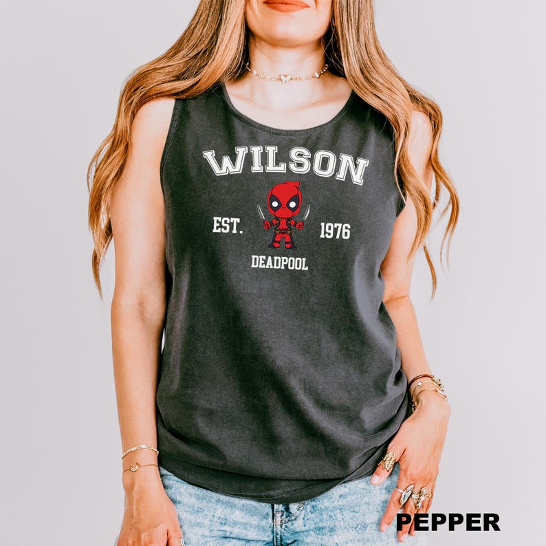 A woman wearing a gray tank top with a graphic of a character from the Marvel Cinematic Universe, specifically Deadpool.