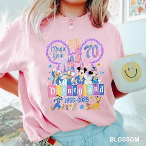 A woman wearing a pink t-shirt with a Disney theme graphic and text, holding a coffee mug with a smiley face.