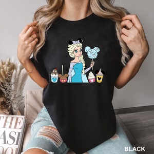 a woman holding up a black shirt with a picture of a princess and cupcake