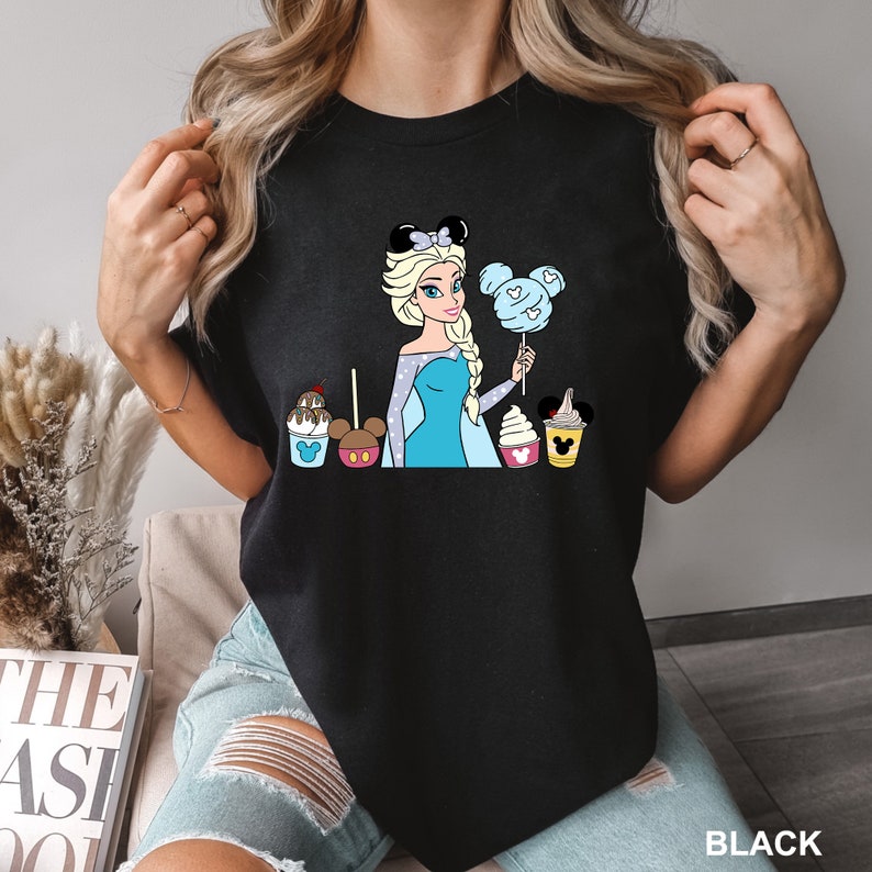 a woman holding up a black shirt with a picture of a princess and cupcake