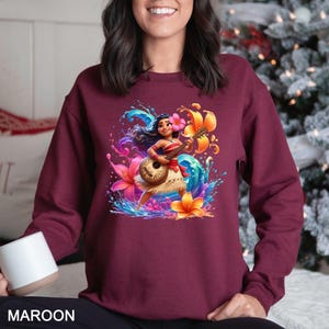 a woman sitting on a bed wearing a maroon sweatshirt