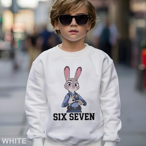 A young boy wearing a white sweatshirt with a cartoon rabbit character and the text "SIX SEVEN" printed on it.