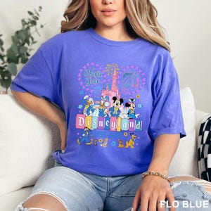 A woman wearing a purple t-shirt with a Disney theme graphic and text, sitting on a couch.