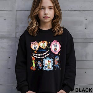 A young girl wearing a black sweatshirt with colorful cartoon characters and designs printed on it.