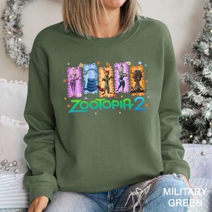 A woman wearing a green sweatshirt with a colorful graphic design featuring characters from the animated film "Zootopia 2".