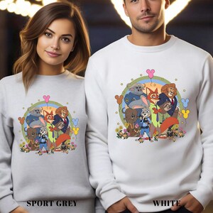 Two people wearing white sweatshirts with a colorful illustration of cartoon animals on them.