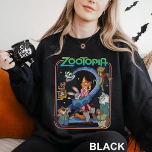 A woman wearing a black sweatshirt with a colorful graphic of the characters from the animated film "Zootopia" on it.