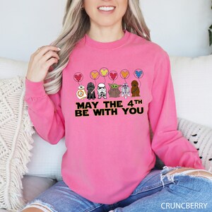 a woman sitting on a couch wearing a pink sweatshirt