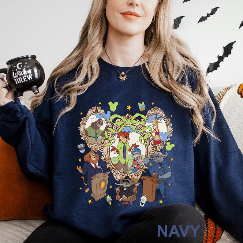 A woman wearing a navy blue sweatshirt with a graphic design featuring cartoon characters from the Disney animated film "Paddington". She is holding a black mug with the text "Witch Brew" printed on it.