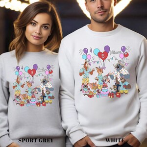 Two people wearing white sweatshirts with a colorful cartoon illustration of animals and a birthday party scene.
