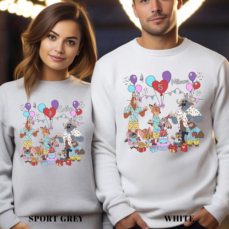 Two people wearing white sweatshirts with a colorful cartoon illustration of animals and a birthday party scene.