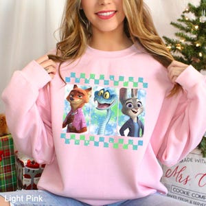 A woman wearing a pink sweatshirt with a graphic of three cartoon animal characters on it.