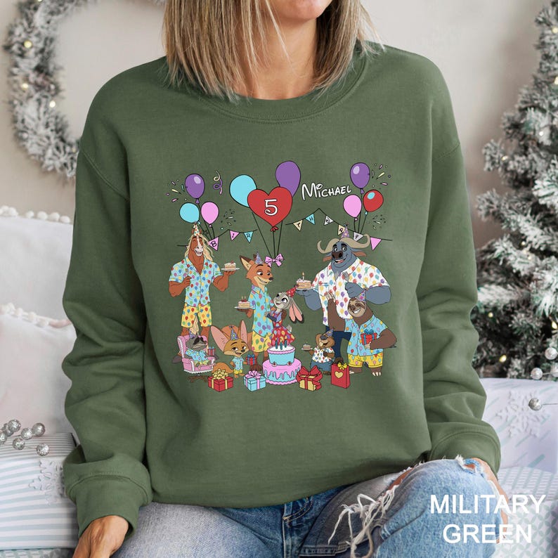 A green sweatshirt with a cartoon illustration of a group of animals celebrating a birthday, surrounded by balloons and presents.
