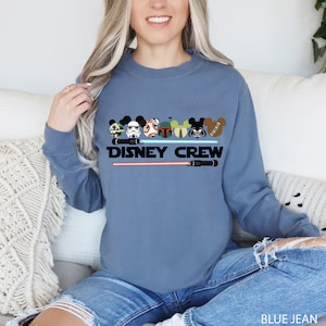 a woman sitting on a couch wearing a disney crew sweatshirt