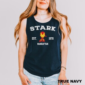 A woman wearing a navy blue tank top with the text "STARK EST. MANHATTAN 1970" and an illustration of Iron Man.
