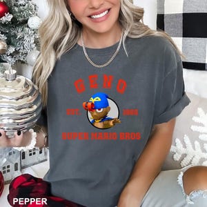 A woman wearing a gray t-shirt with a graphic design featuring a character from the Super Mario Bros. video game franchise.